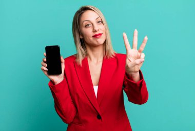 Güzel sarışın kadın gülümsüyor ve arkadaş canlısı görünüyor, üç numarayı gösteriyor. İş kadını telefon ekranı gösteriyor