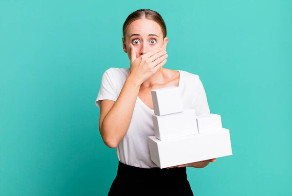 caucasian pretty woman covering mouth with hands with a shocked with white boxes packages