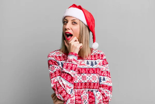 漂亮的金发女人 嘴和眼睛睁得大大的 双手放在下巴上 圣诞和圣诞礼帽的概念 — 图库照片