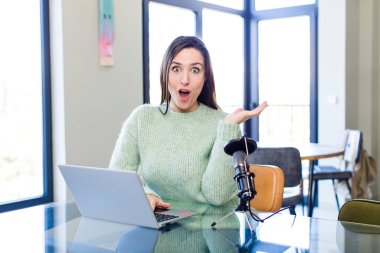 young pretty woman looking surprised and shocked, with jaw dropped holding an object. influencer concept