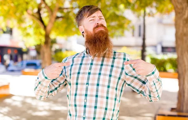 red hair bearded man with a bad attitude looking proud and aggressive, pointing upwards or making fun sign with hands
