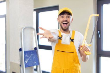 Genç yakışıklı adam mutlu bir şekilde gülümsüyor ve bir konsept sunuyor ya da gösteriyor. Testereli tamirci.