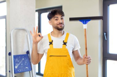 Genç yakışıklı adam kendini mutlu hissediyor, iyi bir jestle onaylıyor. pencere temizleme konsepti