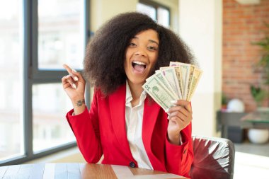Güzel afro siyah kadın bir fikri fark ettikten sonra mutlu ve heyecanlı bir dahi gibi hissediyor. Dolar banknotları konsepti