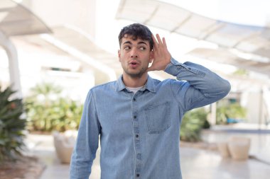 Genç yakışıklı adam ciddi ve meraklı görünüyor, dinliyor, gizli bir konuşma veya dedikodu duymaya çalışıyor, kulak misafiri oluyor.