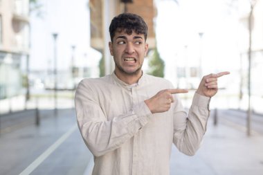 Genç yakışıklı adam şaşkın ve şaşırmış hissediyor. Kenardaki fotokopi alanını işaret ediyor. Şaşırmış, ağzı açık bir bakış.