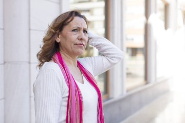 Orta yaşlı kadın şaşkın ve şaşkın hissediyor, kafasını kaşıyor ve yan tarafa bakıyor.