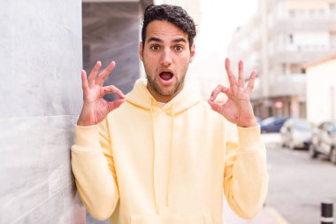 Genç İspanyol adam şok olmuş, şaşırmış ve şaşırmış hissediyor. Onaylıyor. İki eliyle işaret veriyor.