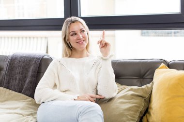 Genç ve güzel bir kadın mutlu bir şekilde gülümsüyor ve yan bakıyor, merak ediyor, düşünüyor ya da bir kanepede oturuyor.