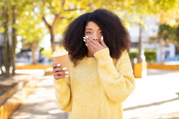 Güzel afro siyah bir kadın ağzını eliyle kapatıyor ve şok olmuş ya da şaşırmış bir ifade takınıyor. kahve konseptini kaldır.