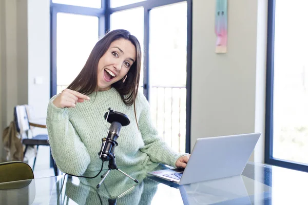 young pretty young adult influencer woman with a microphone and a laptop on a desk