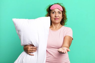 Sevimli orta yaşlı bir kadın mutlu bir şekilde gülümsüyor ve pijama giyip yastık takarak bir konsept sunuyor.