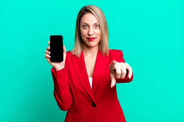 Güzel sarışın kadın seni seçen kamerayı işaret ediyor. İş kadını telefon ekranı gösteriyor