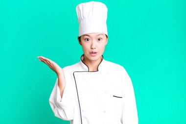 Güzel Asyalı kadın şaşırmış ve şok olmuş görünüyor. Çenesi düşmüş ve elinde bir nesne var. restoran şefi konsepti