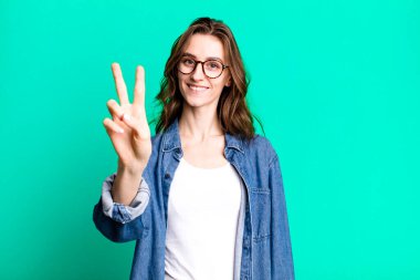 Gülümseyen ve mutlu görünen genç güzel bir kadın zafer ya da barış işareti yapıyor.