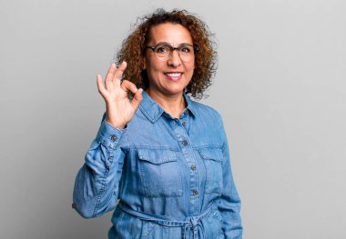 Orta yaşlı İspanyol kadın mutlu, rahat ve tatmin olmuş hissediyor. Onayını iyi bir hareketle gösteriyor. Gülümsüyor.