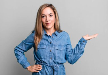 blonde adult woman smiling, feeling confident, successful and happy, showing concept or idea on copy space on the side