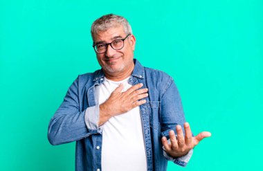 Orta yaşlı bir adam mutlu ve aşık, bir eli kalbinin yanında, diğer eli önde.