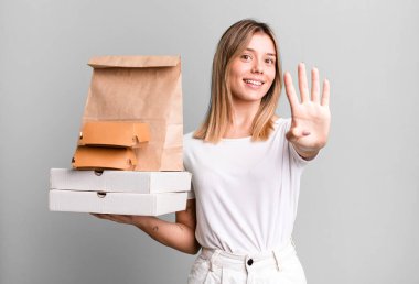 Genç, güzel bir bayan gülümsüyor ve arkadaş canlısı görünüyor, dört numarayı gösteriyor. Yemek teslimatı ve paket servis.