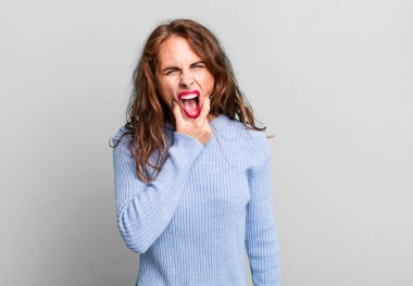 Ağzı ve gözleri açık, eli çenesinde genç ve güzel bir kadın. Hoş olmayan bir şok geçiriyor.