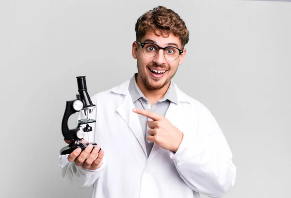 若い大人の白人男性が興奮し 側を指して驚いています 顕微鏡の概念を持つ科学研究室の学生は — ストック写真