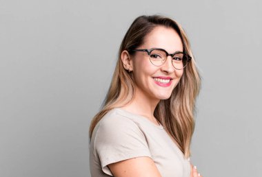 Kameraya çapraz kollarla gülümsüyor ve mutlu, kendinden emin, tatmin olmuş bir ifade, yan görüş.