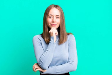 Mutlu görünüyor ve gülümsüyor, elleri çenesinde, merak ediyor ya da bir soru soruyor, seçenekleri karşılaştırıyor.