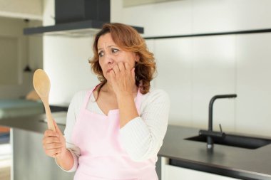 Orta yaşlı, güzel bir kadın korkmuş, endişeli ya da kızgın hissedip yan tarafa bakıyor. ev konseptinde yemek yapmak