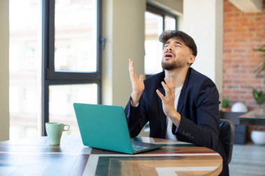 Genç yakışıklı adam ellerini havaya kaldırarak çığlık atıyor. Dizüstü bilgisayarla serbest konsept