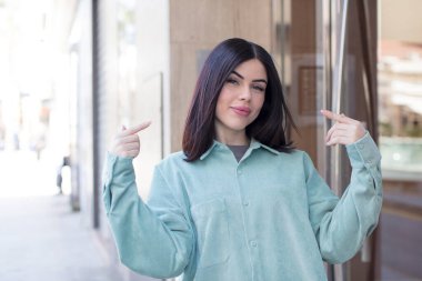 Genç, güzel bir kadın, kendine güvenerek gülümsüyor. Kendi gülüşünü gösteriyor. Olumlu, rahat, tatmin olmuş bir tavır.