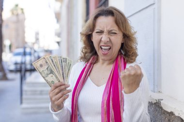 Orta yaşlı, güzel bir kadın sinirli, sinirli ve sinirli görünüyor. Dolar banknotları konsepti