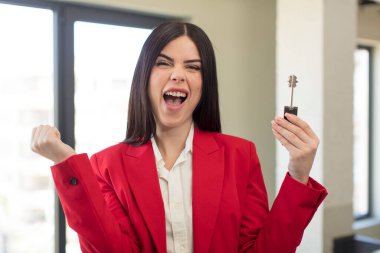 Güzel genç bir kadın şok olmuş hissediyor, gülüyor ve başarıyı kutluyor. yeni ev anahtarı kavramı