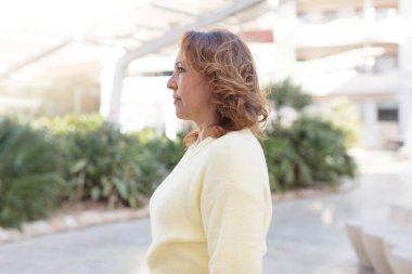 Profil görünümlü orta yaşlı kadın ileriyi kopyalamak istiyor, düşünüyor, hayal ediyor ya da hayal kuruyor.