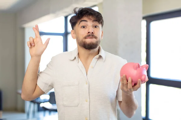 Young Handsome Man Crossing Fingers Hoping Good Luck Piggy Bank — Stock Photo, Image