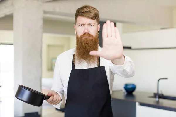 红头发的男人看上去很严肃 在厨房里摆出了张开的手心 摆出了个停下来的姿势 厨师概念 — 图库照片