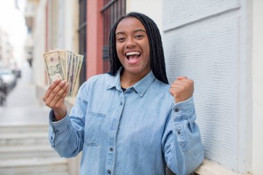 Siyah afro kadın şokta, gülüyor ve başarıyı kutluyor. Dolar banknotları konsepti