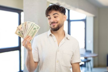 Genç ve yakışıklı bir adam gülümsüyor ve kendine güveni tam bir ifadeyle bakıyor. Dolar banknotları konsepti