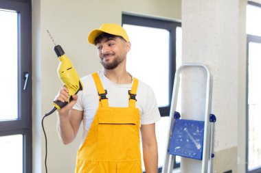 Genç ve yakışıklı bir adam gülümsüyor ve kendine güveni tam bir ifadeyle bakıyor. Tamirci ve matkap konsepti