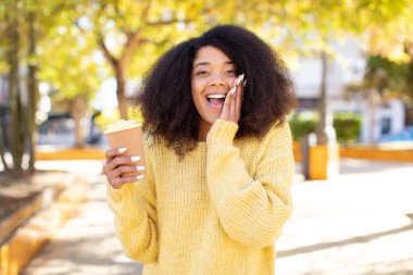 Oldukça afro siyah bir kadın inanılmaz bir şey karşısında mutlu ve şaşkın hissediyor. kahve konseptini kaldır.