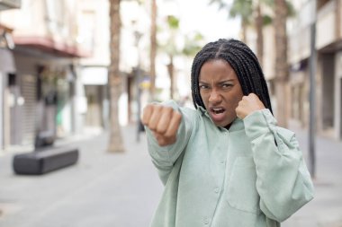 Afro güzel siyah kadın kendinden emin, sinirli, güçlü ve agresif görünüyor. Yumrukları boks pozisyonunda dövüşmeye hazır.