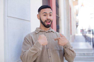 Genç yakışıklı adam mutlu, gururlu ve şaşırmış görünüyor, neşeli bir şekilde kendini gösteriyor, kendinden emin ve yüce hissediyor.