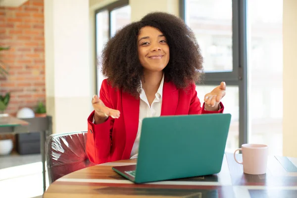 pretty afro black woman smiling cheerfully, feeling happy and showing a concept. businesswoman and laptop concept