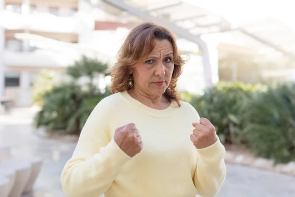 middle age woman looking confident, angry, strong and aggressive, with fists ready to fight in boxing position