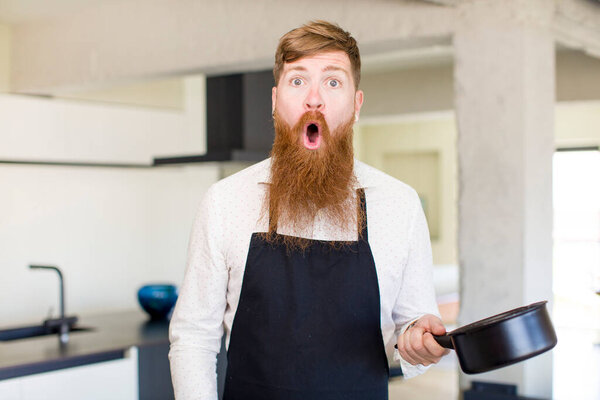 red hair man feeling extremely shocked and surprised in a kitchen. chef concept