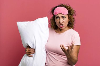 Güzel, orta yaşlı bir kadın sinirli, sinirli ve sinirli görünüyor pijama geceliği ve yastık giyiyor.