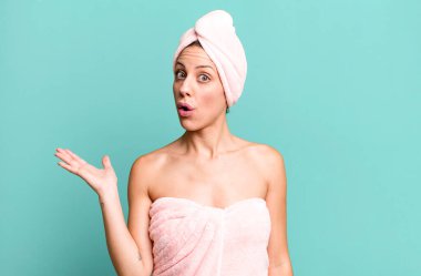 Güzel sarışın kadın şaşırmış ve şok olmuş görünüyor. Çenesi düşmüş ve elinde bir nesne var. Bornoz ve güzellik konsepti