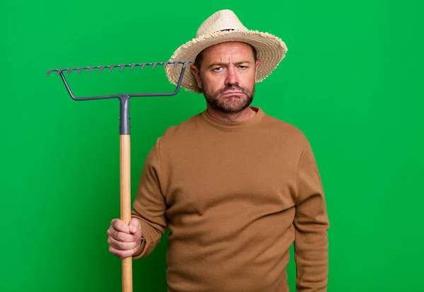 middle age man feeling sad and whiney with an unhappy look and crying. farmer with a rake