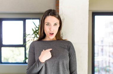 young adult pretty woman looking shocked and surprised with mouth wide open, pointing to self