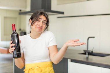 Genç bir kadın omuz silkiyor, kafası karışık ve kararsız. şarap şişesi konsepti