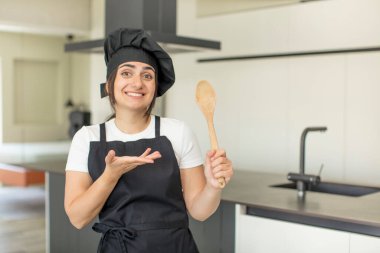 Genç bir kadın neşeyle gülümsüyor, mutlu hissediyor ve bir konsept gösteriyor. Şef konsepti